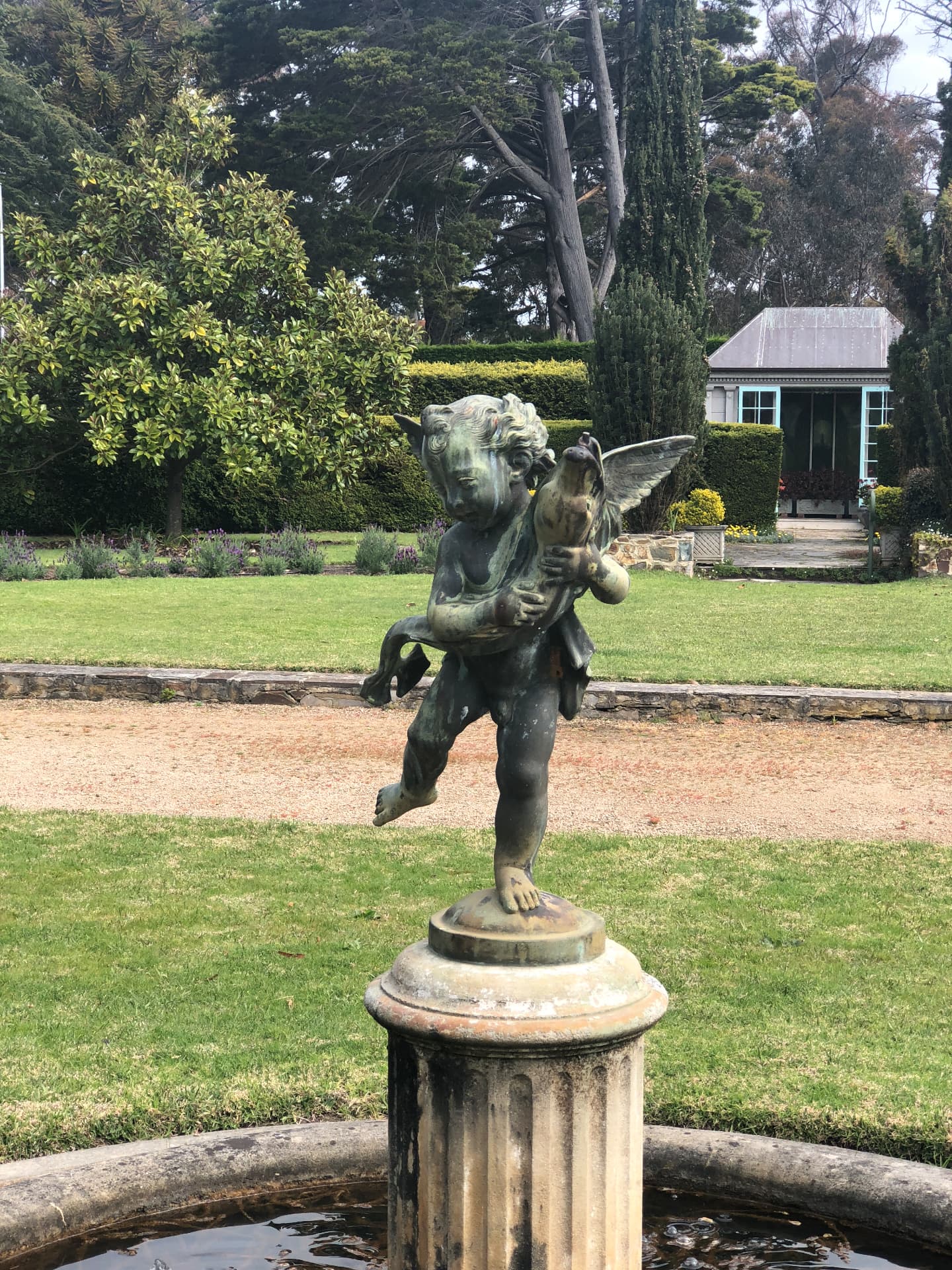Bronze cherub statue in the mansion's garden with hedges and lawn