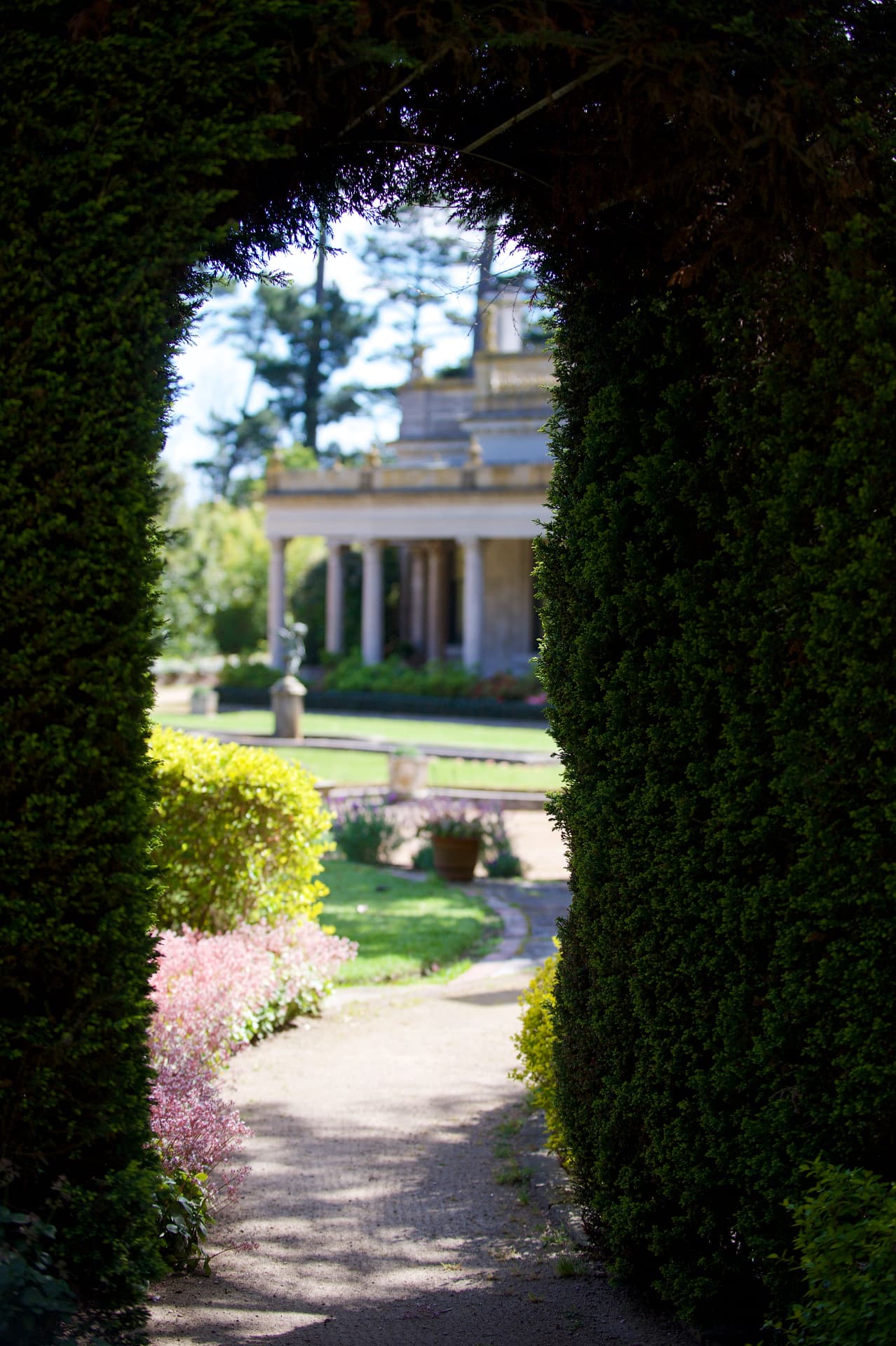 Garden path leading through a hedge arch toward the colonnaded mansion