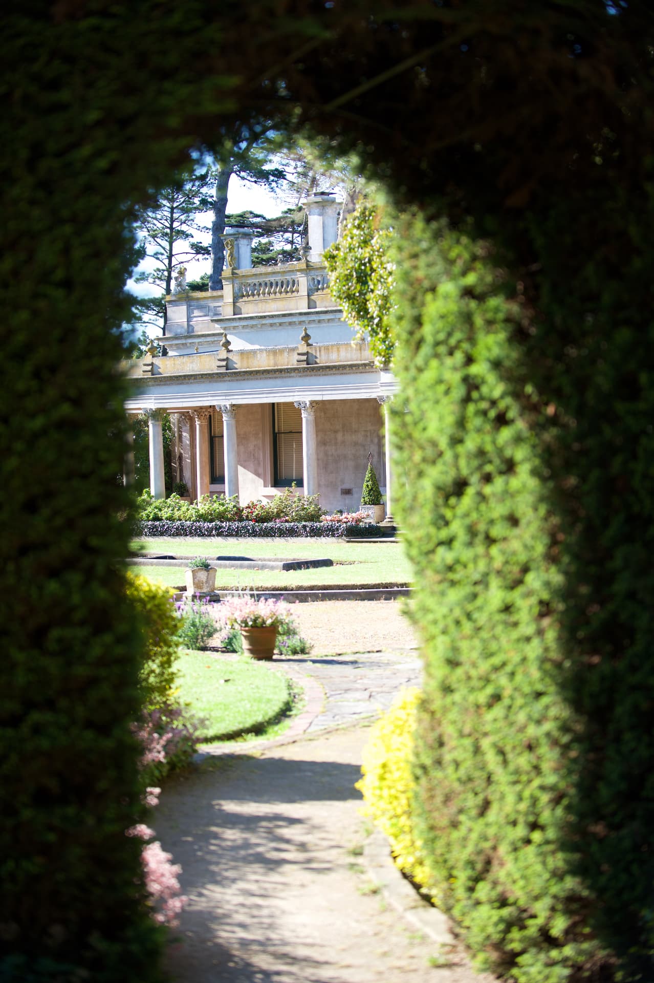 View of the mansion framed by a clipped hedge archway and garden path