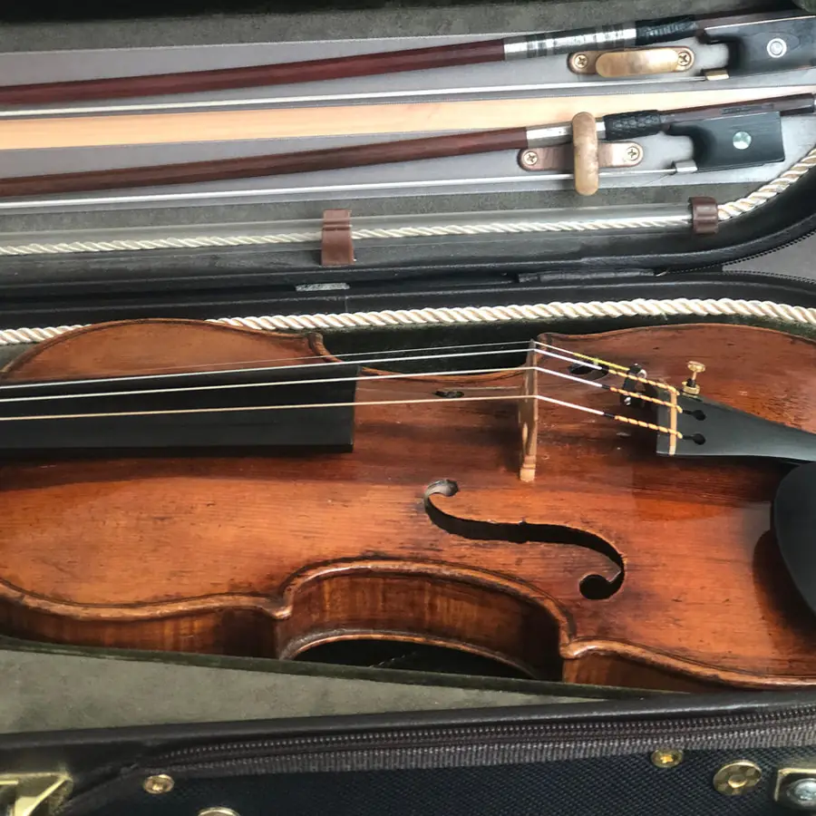 A violin lying in its open case with two bows above it